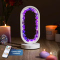 Lit white oval lamp edged with amethyst crystals, with remote beside candles