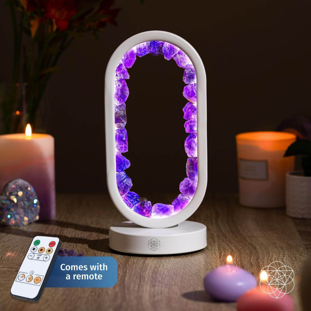 Lit white oval lamp edged with amethyst crystals, with remote beside candles